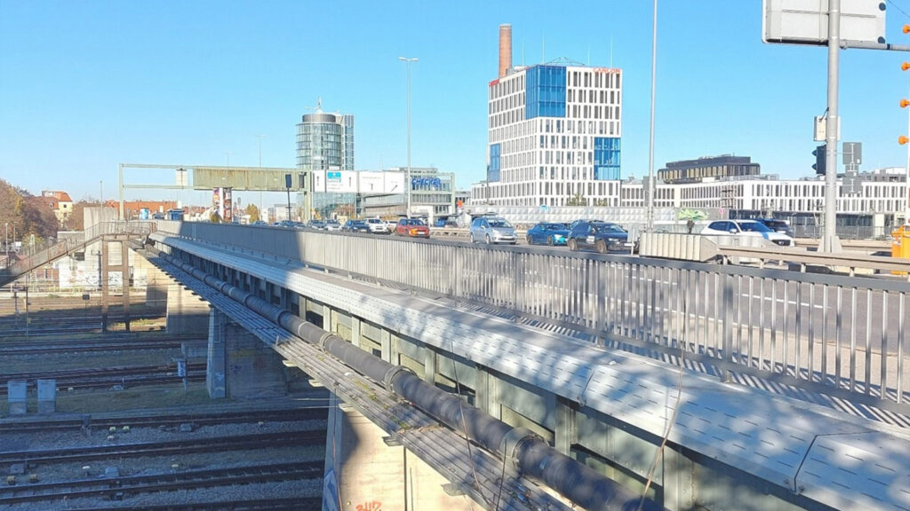 Eine Brücke, über die Autos fahren. Darunter Bahngleise, im Hintergrund Hochhäuser.