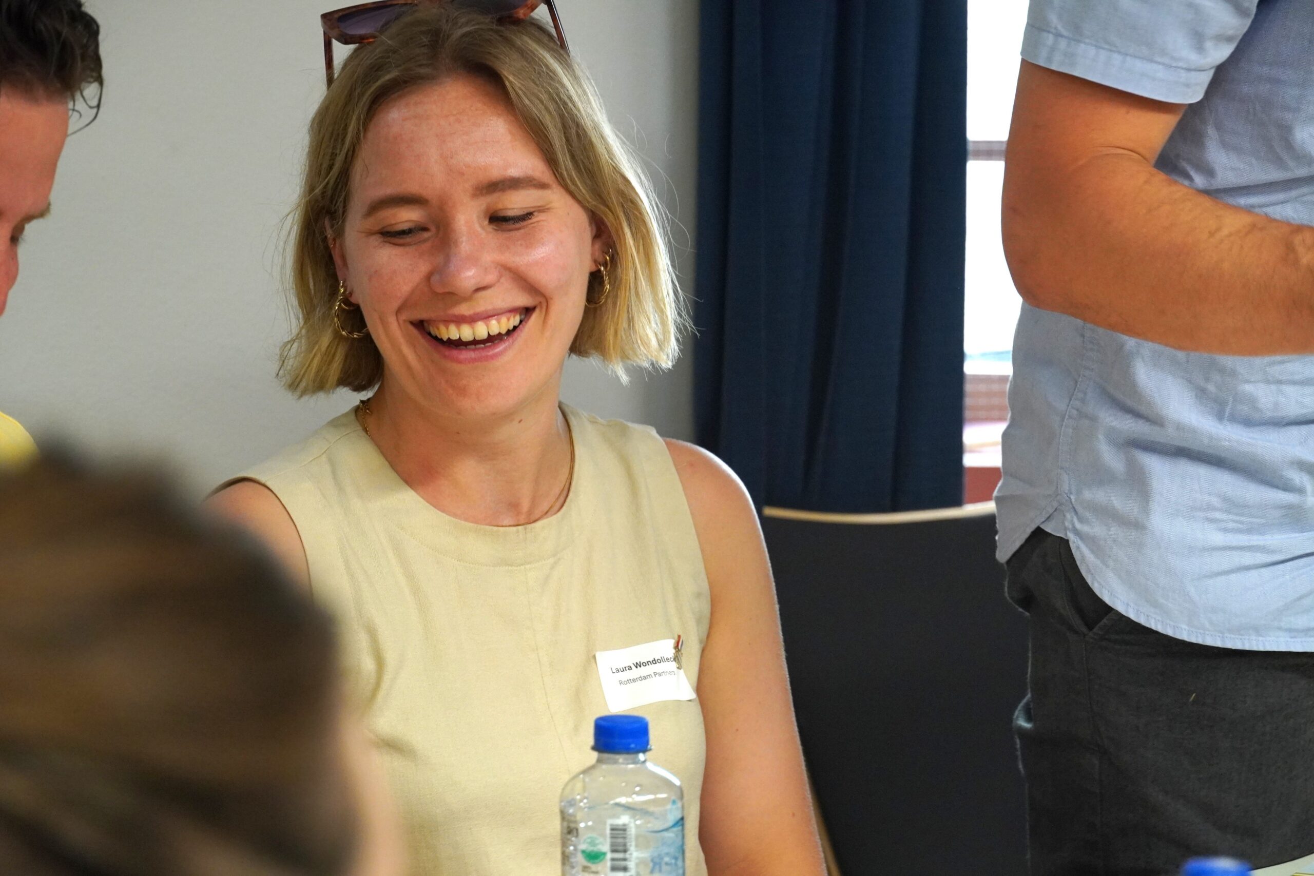Eine Frau mit blonden Haaren und beigefarbener Bluse, die lacht