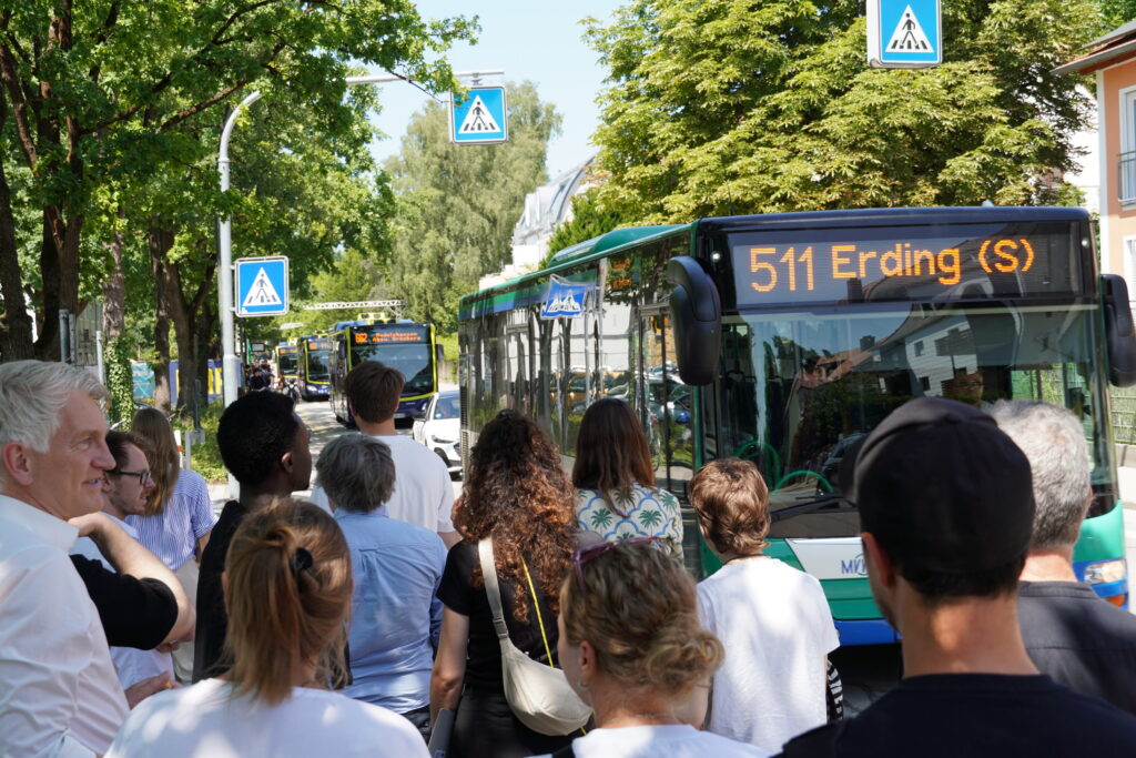 An einem Zebrastreifen rollen mehrere Busse und Autos heran, vorn im Bild drängen sich Fußgängerinnen und Fußgänger.