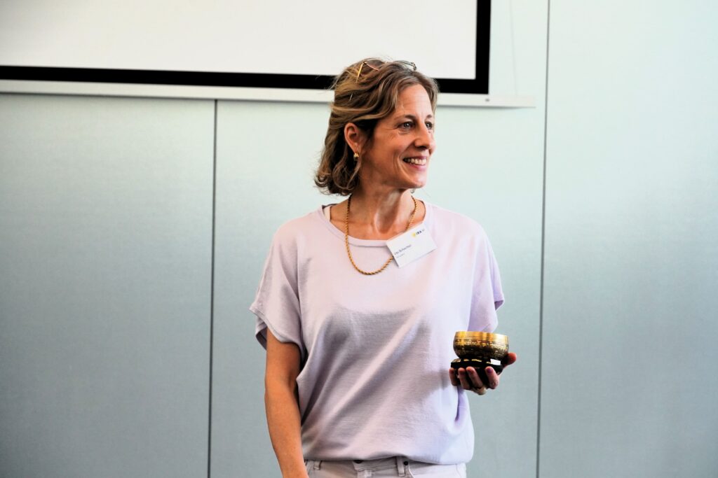 Eine Frau mit hellen Haaren sieht lächelnd nach rechts in ihrer Hand eine Klangschale.
